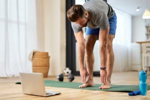 Athletic young man doing exercise and using laptop at home